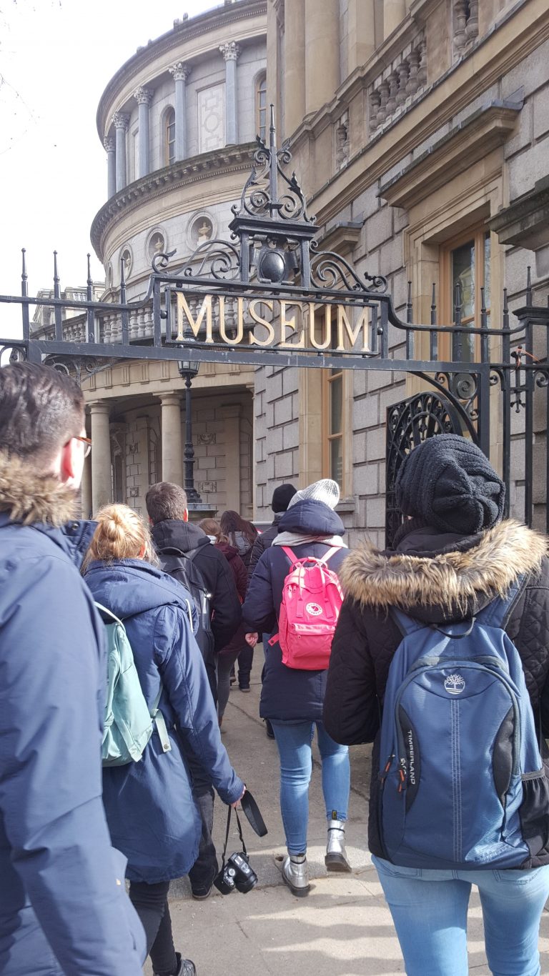 Mehrere Personen vin Hinten zu sehen, gehen durch ein Tor mit dem Schriftzug "Museum"